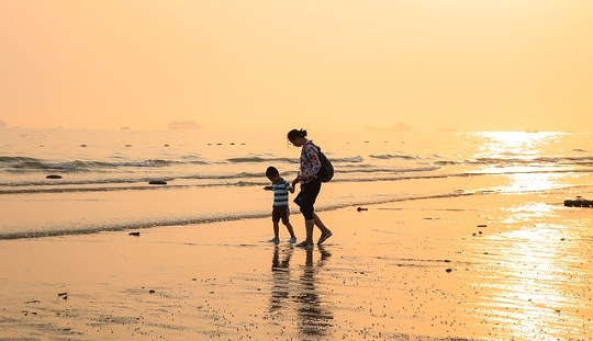 child and adult walking hand in hand on a beach