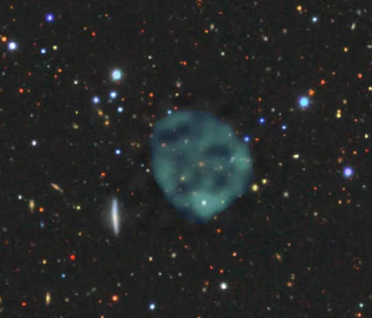 The ghostly ORC1 (blue/green fuzz), on a backdrop of the galaxies at optical wavelengths. 