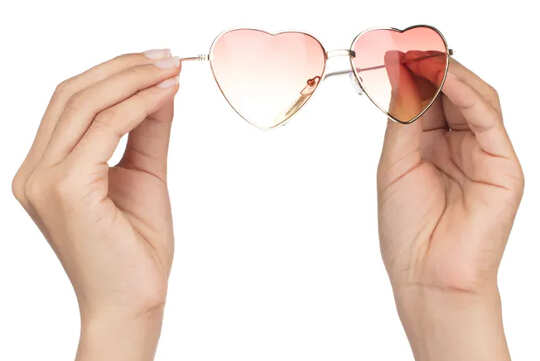 hands holding heart-shaped rose-colored glasses