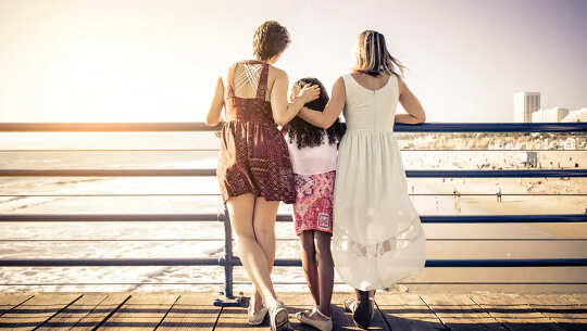 two women with a child in the middle standing at a railing looking out at nature