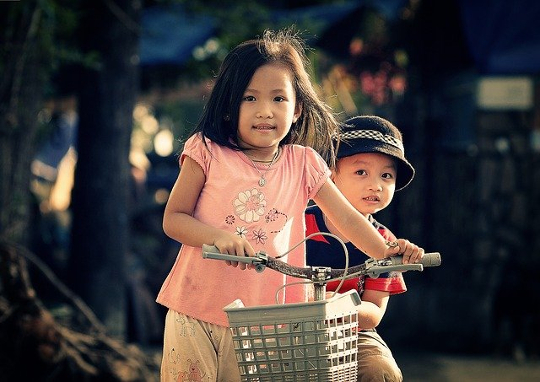 young girl on a bicycle with her brother sitting behind her