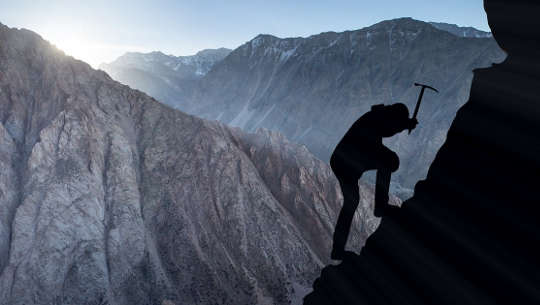 photo silhouette of mountain climber using a pick to secure himself