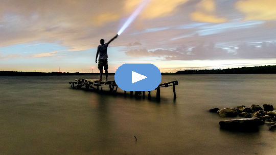 man standing on a dock shining a flashlight into the sky