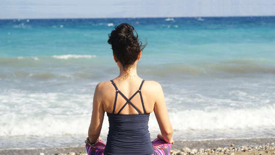 view from the back of a woman sitting on the beach in meditation