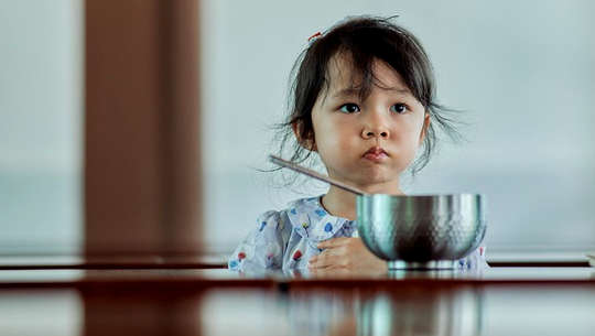 unhappy child sitting in front of a bowl of food