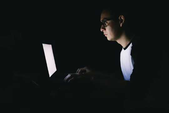 Young man working on his laptop in the dark.