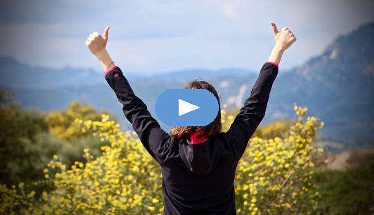 woman looking out over a valley with her two hands in the air with thumbs up