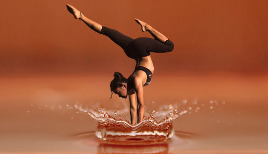a woman in a hand-stand yoga pose in water