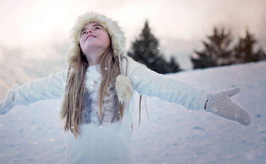 young girl smiling with arms open to the sky in the middle of a snowy landscape