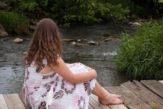 young barefoot woman sitting on a bridge looking out at the river