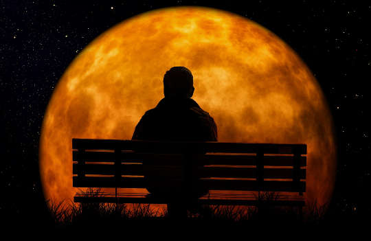 a person sitting on a bench in front of a huge full moon