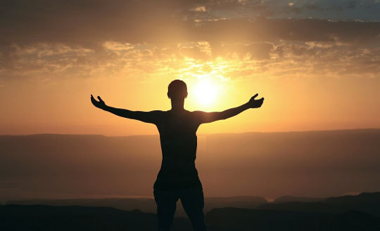 a person with wide open arms facing the rising sun