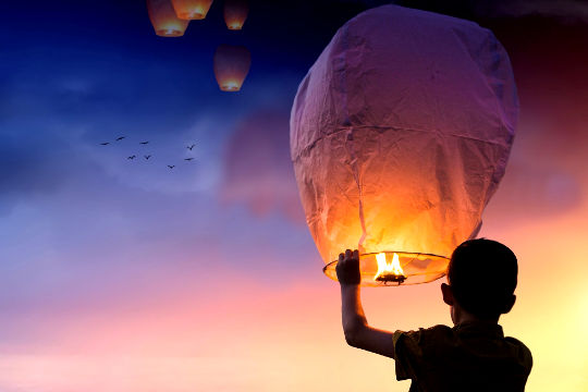 a young boy releasing lit-up balloons into the sky