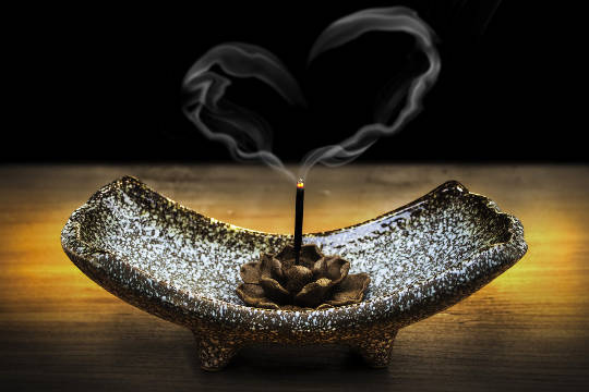 the smoke from a burning incense stick rises up in the shape of a heart