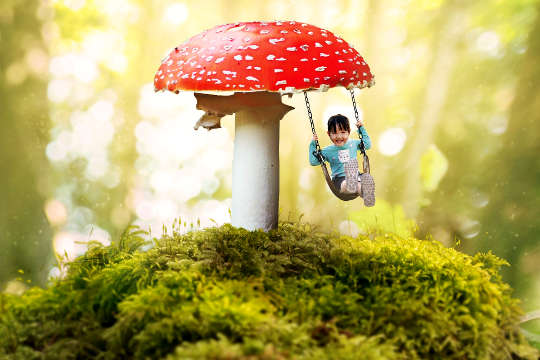 a child on a swing handing from a huge red mushroom