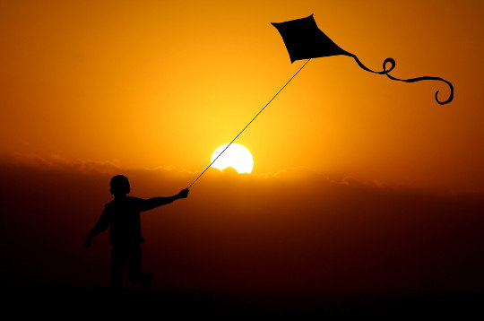 a child flying a kite at sunset