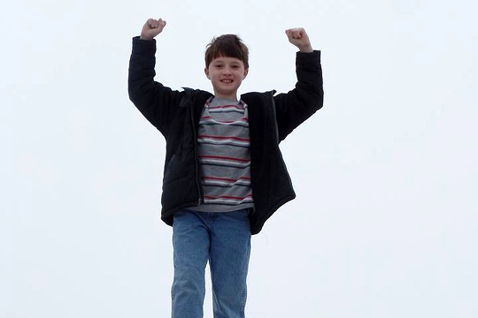 a young boy standing with his arms raised in victory