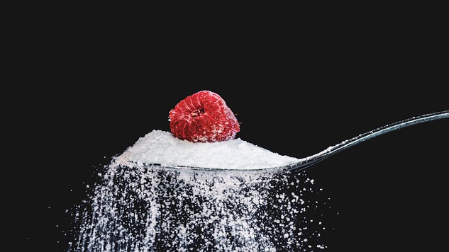 a raspberry sitting on top of a teaspoon of sugar