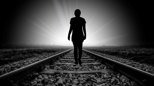 silhouette of a person walking on a railroad track towards the light