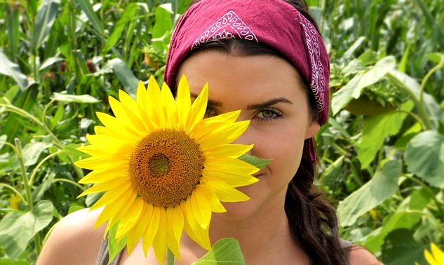 a woman standing slightly behind a sunflower that is as big as her head