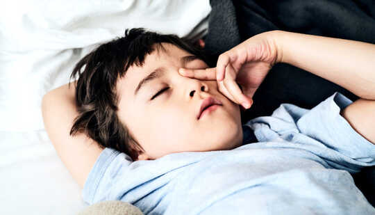 A young boy rubs his eye as he lays in bed