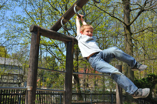 Child swings from monkey bars at a playground.