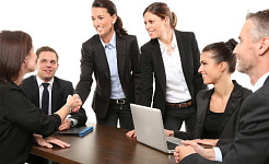 women shaking hands at a business meeting, with men loooking on