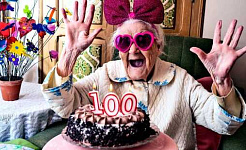 A woman looks excited with pink glasses and a bow on, looking at a cake with