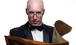 a man wearing a bow-tie and reading glasses while holding an open newspaper