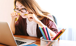 young woman at her laptop biting down hard on a pencil
