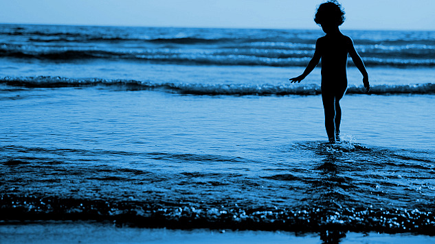young boy standing in the water at the edge of the waves rippling in