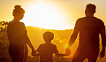 a couple holding hands of their child facing the setting sun