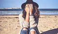 young woman sitting on a beach with her face hidden in her bands