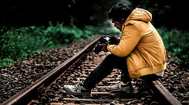 young man sitting on the railroad tracks looking at the pictures in his camera