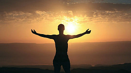 a person with wide open arms facing the rising sun