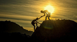 two climbers, with one giving the other a helping hand