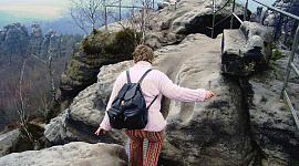 older woman wearing a backpack climbing a rocky path