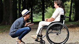 caring person squatting down in front of another in a wheelchair