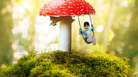 a child on a swing handing from a huge red mushroom