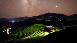 bright light from under small building light terraced rice fields under starry sky